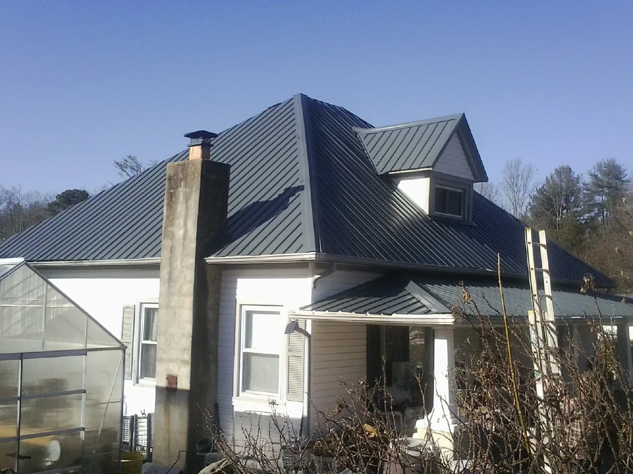 Dark blue standing seam metal roof on a white farmhouse with dormer — Slate & Tile Roof Repair by Roofing Brothers in Brooklyn